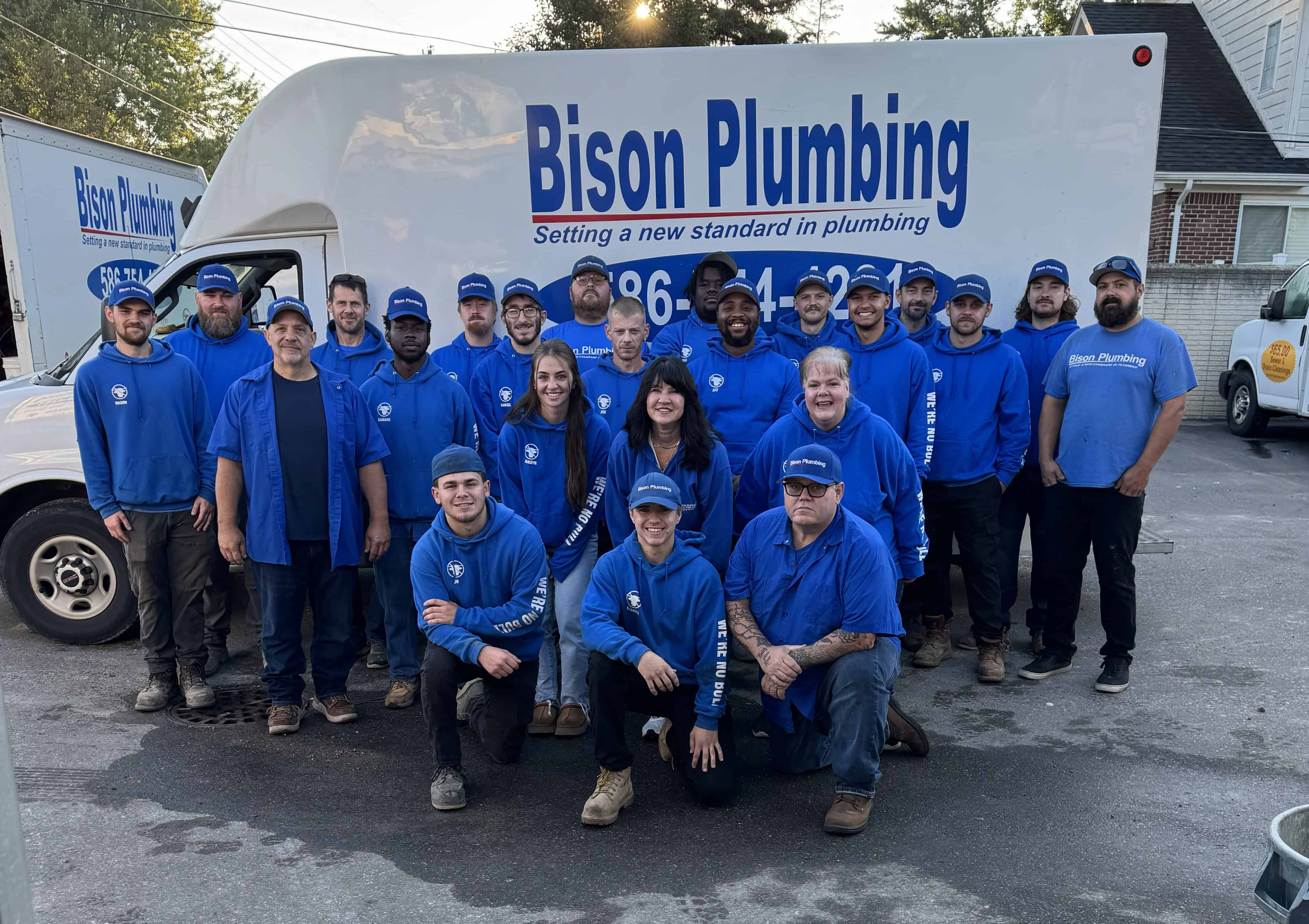 The Bison Plumbing team in blue company shirts and hats standing together in front of a branded Bison Plumbing service van