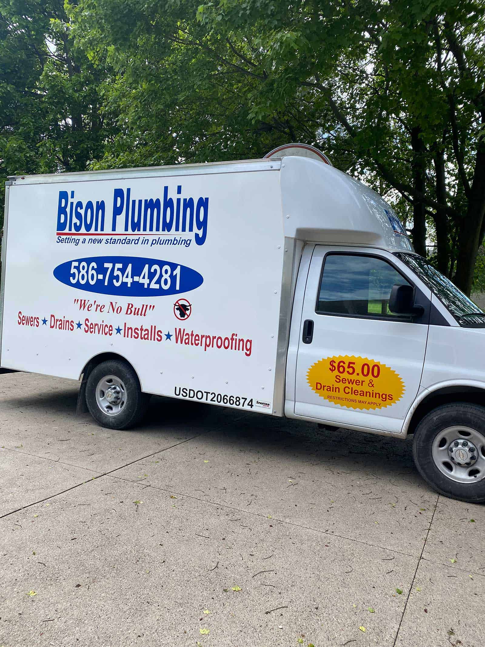 A branded Bison Plumbing box truck with the company phone number, parked on a Michigan residential job