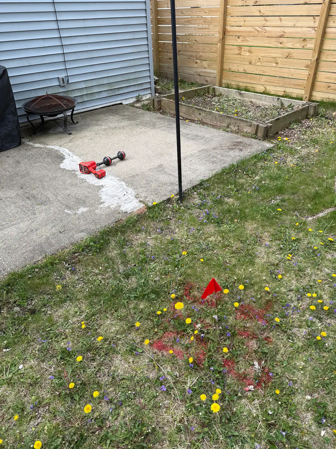 Exterior crawlspace access hatch below a brick foundation wall with a length of white PVC pipe and a tool case staged at the opening