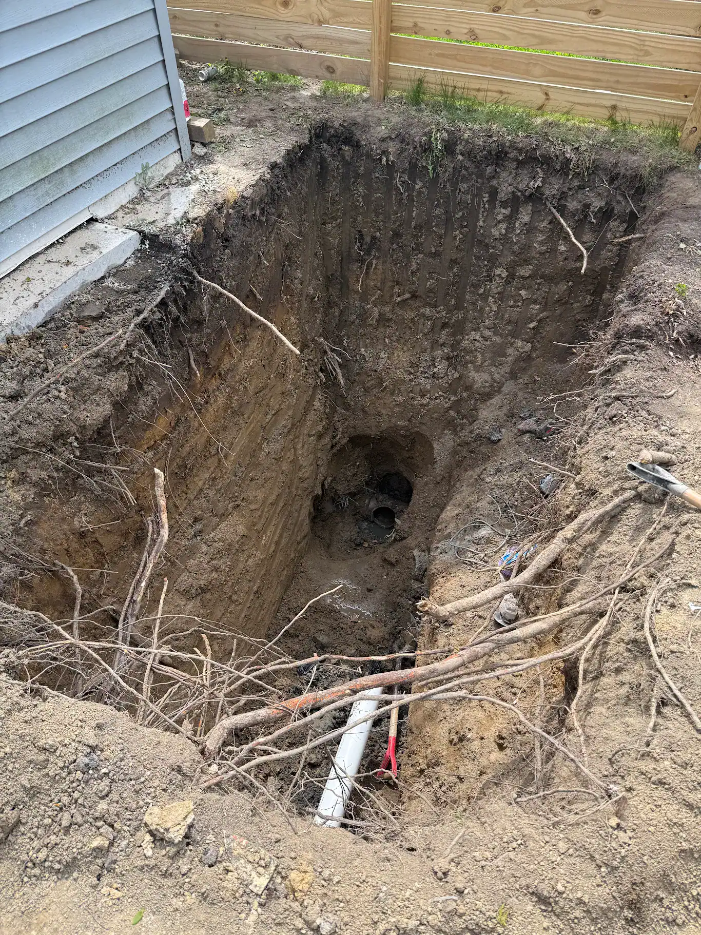New white PVC trunk drain line running the length of a sand crawlspace beneath floor joists and ductwork